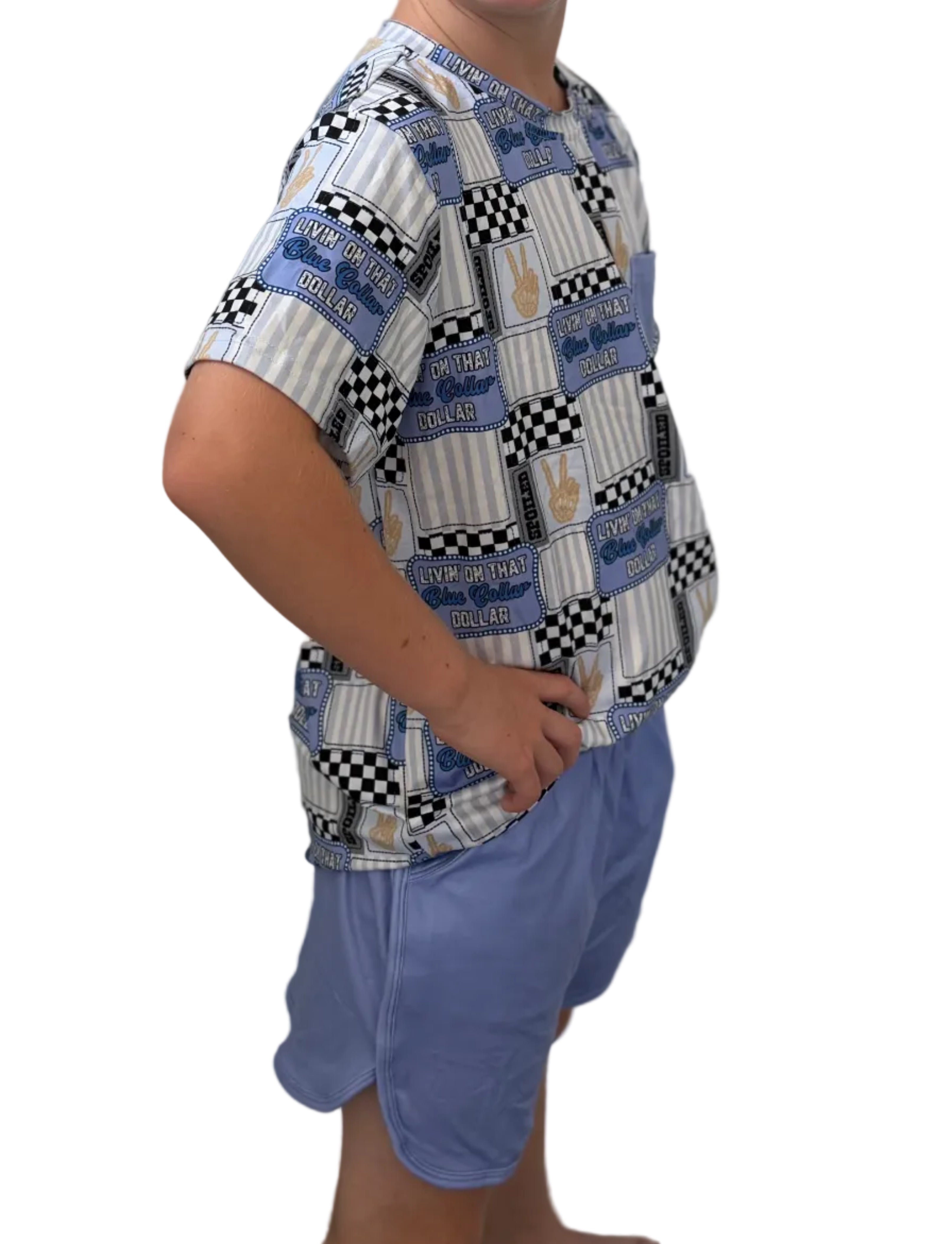 Young boy wearing a patterned shirt and blue shorts against a plain wall.