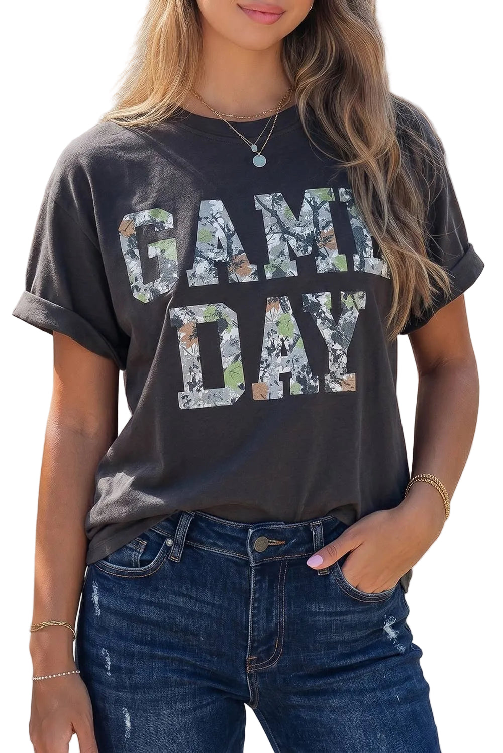 A woman wearing a dark charcoal gray t-shirt with 'GAME DAY' printed in camouflage-patterned letters, paired with blue jeans.